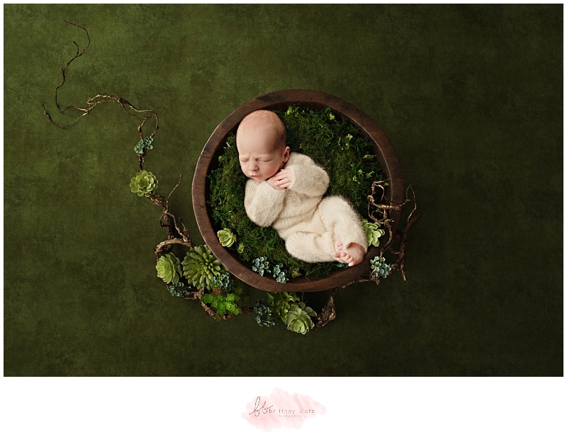 Baby boy in white knit outfit sleeping in bow with greenery