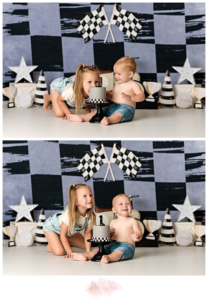 One year old boy and big sister smiling in front of race-themed cake smash set