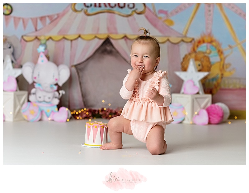 Baby girl smiling with cake in her mouth during her circus-themed cake smash in calgary