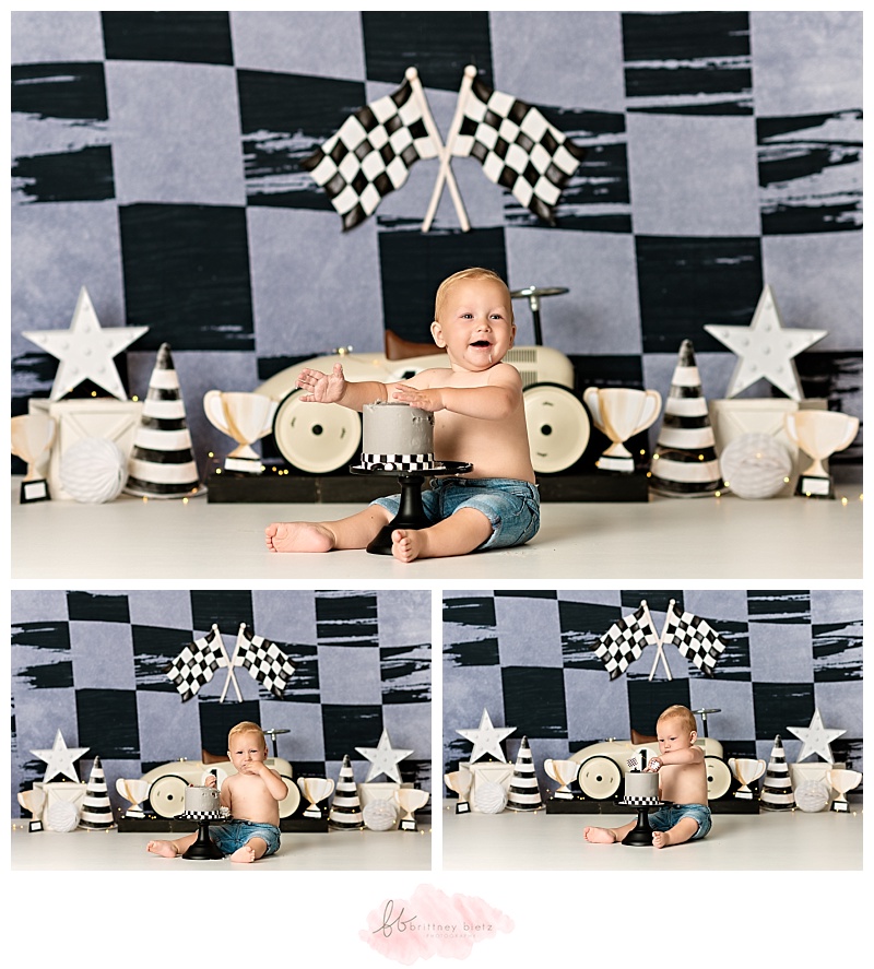 One year old boy sitting with cake smiling in front of race-themed cake smash set