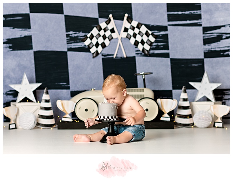 One year old boy sitting with face in cake in front of race-themed cake smash set