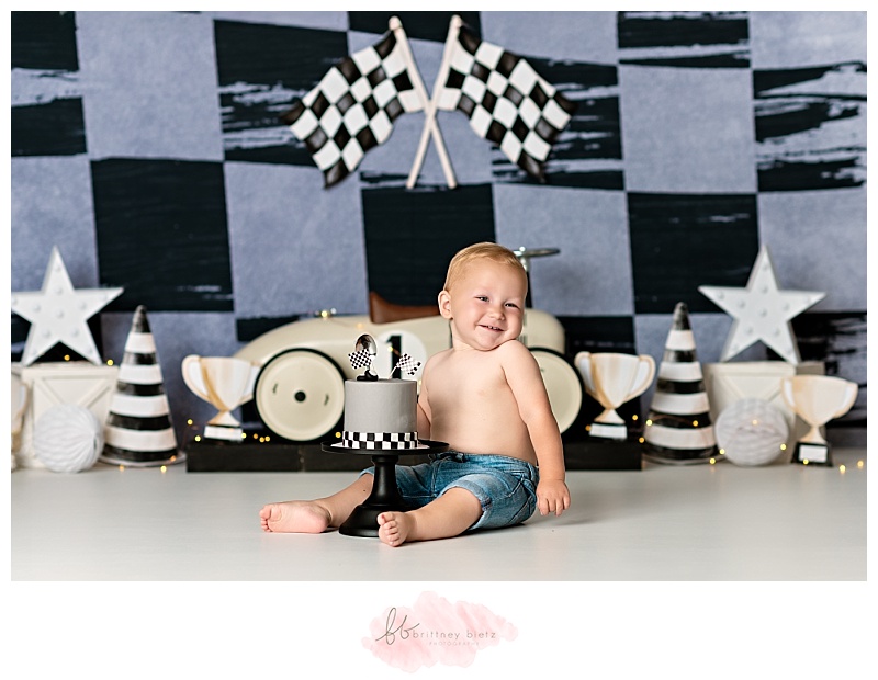 One year old boy sitting and smiling in front of race-themed cake smash set