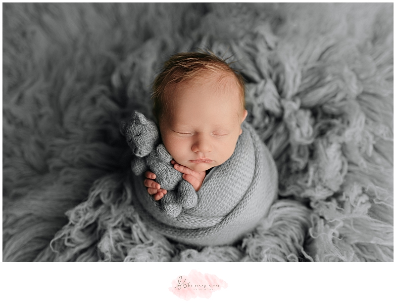 newborn baby boy in potato sack pose with stuffed teddy bear on grey flokati