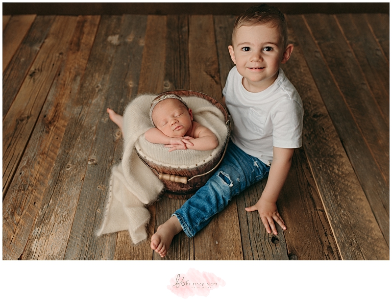 Baby sister in bucket beside smiling big brother