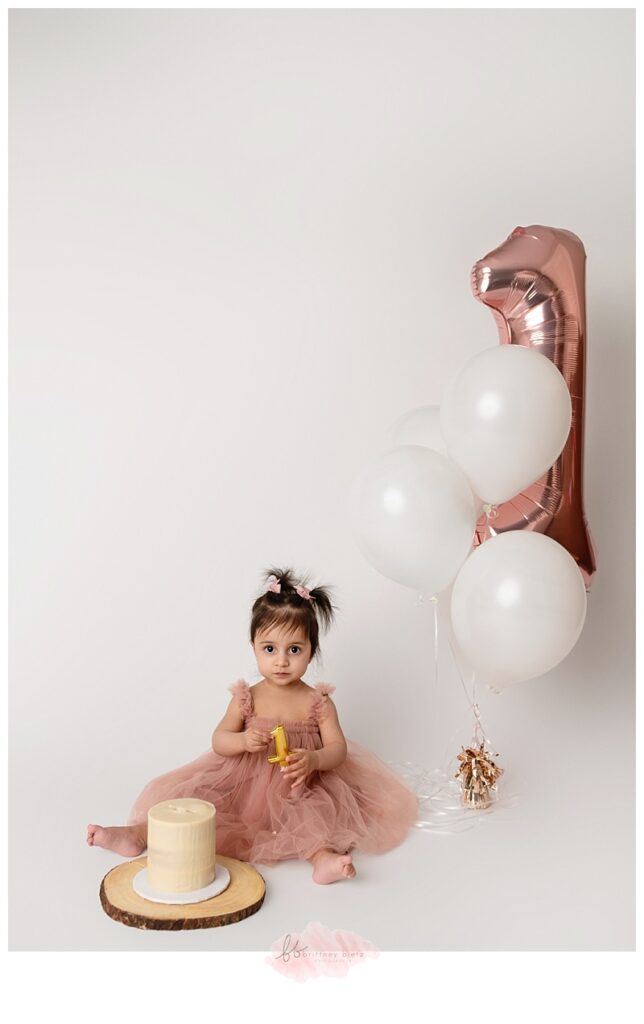 Baby gently exploring her birthday cake with her fingers during a cake smash photography session.
