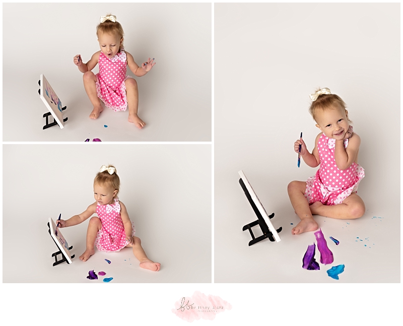 2-year old girl in pink polka dot apron excitedly painting on canvas
