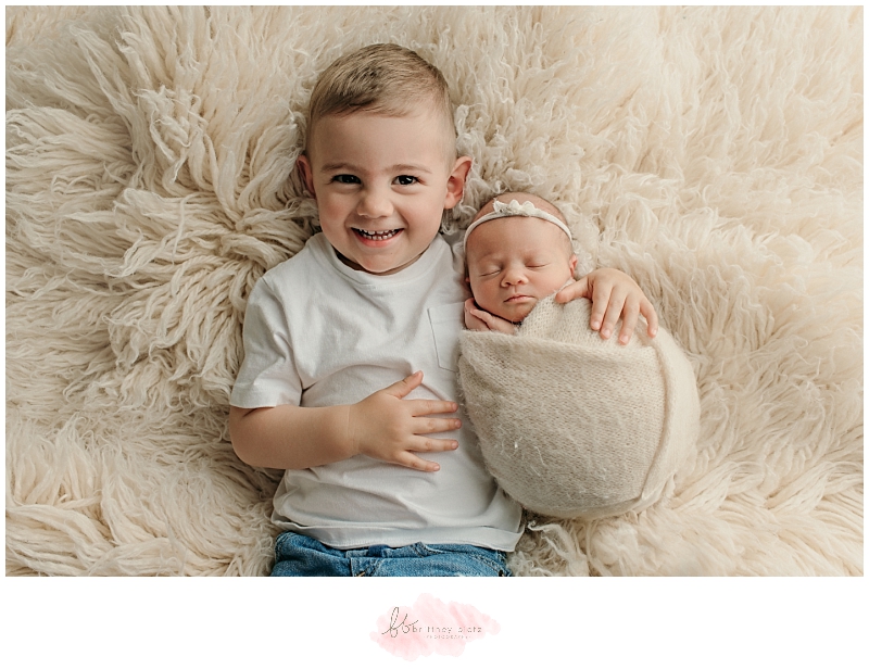 Baby sister cuddled up with smiling bit brother