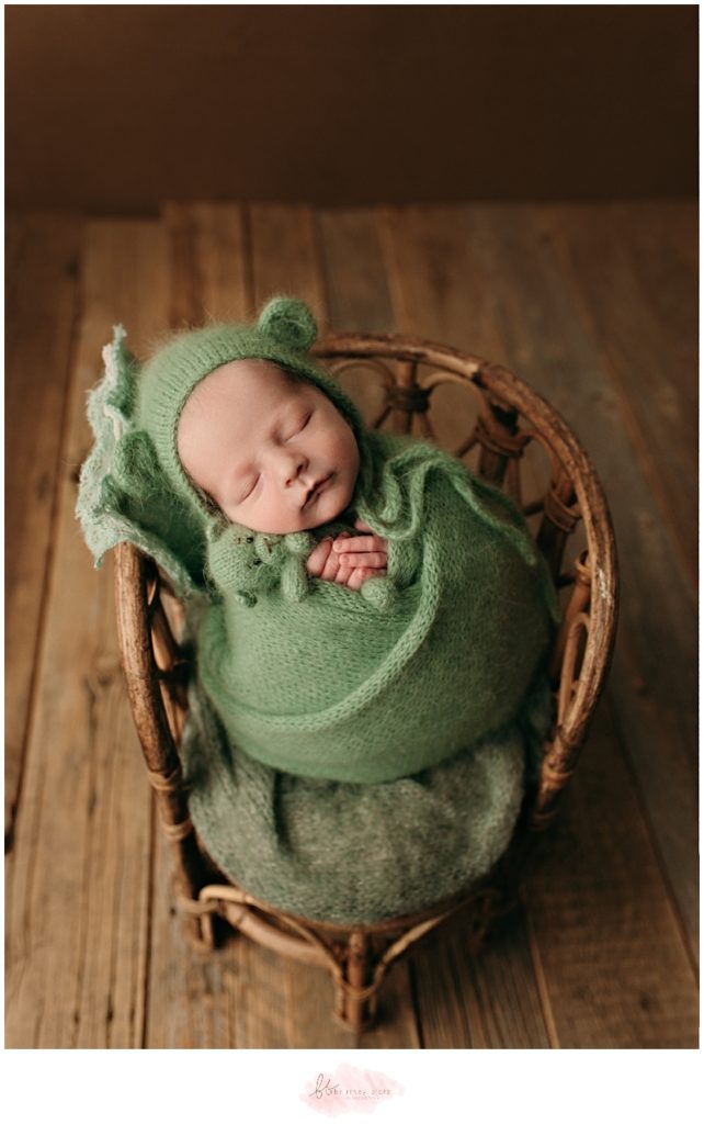 Newborn baby boy wrapped in green holding bear on chair