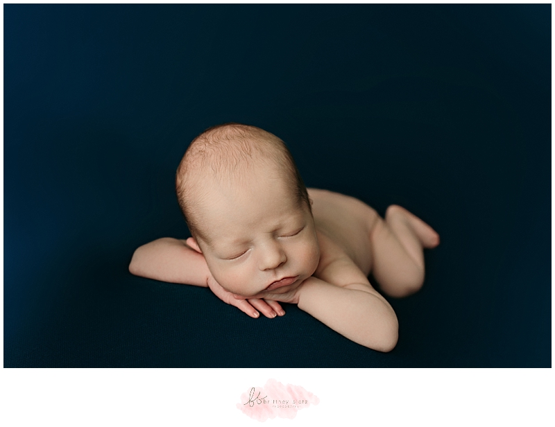 Baby boy sleeping on navy blue fabric in head on hands pose