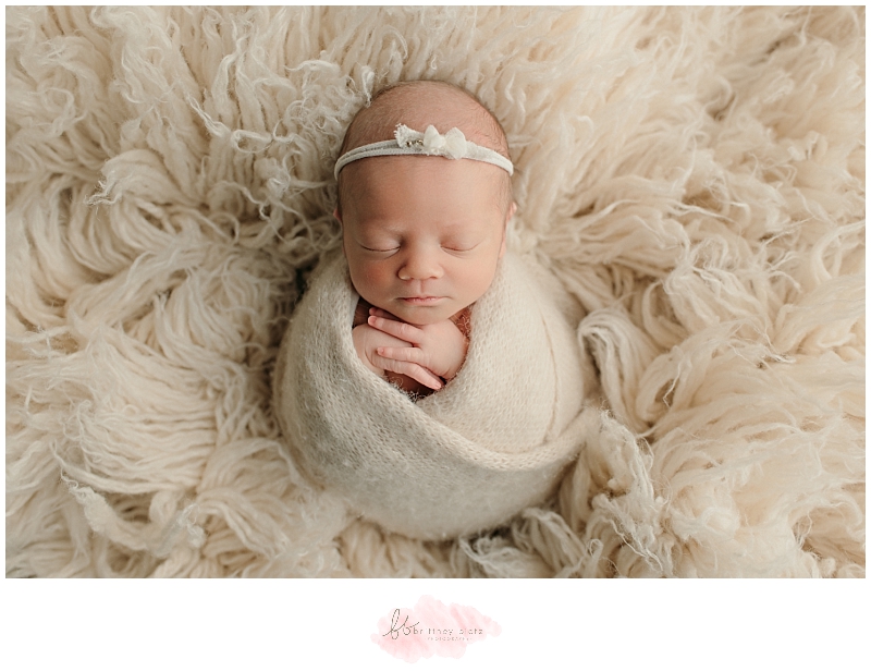 Newborn baby girl wrapped in white knit layer on flokati rug