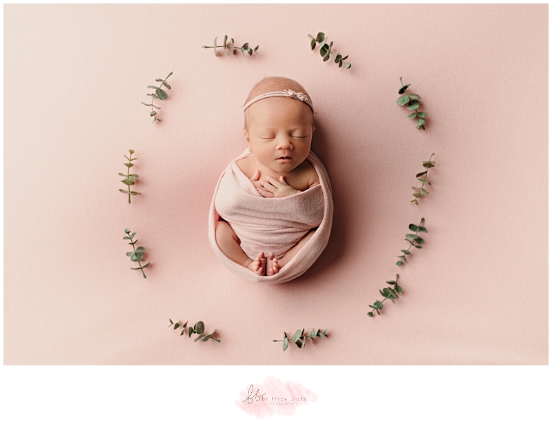 Newborn baby girl wrapped in pink surrounded by leaves